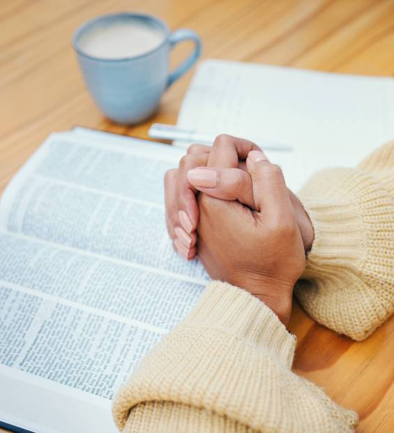 Hands, bible and praying at table, religion and Christian worship in home at desk. Closeup, holy bo.